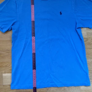 Blå t-shirt från Ralph Lauren - Snygg blå t-shirt från Polo Ralph Lauren med klassisk passform och korta ärmar. T-shirten har en broderad marinblå logga på bröstet och är tillverkad i mjuk bomull. 