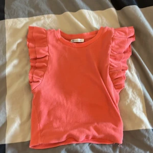 Rosa volangtopp från Zara - Supersöt rosa topp från Zara med volangdetaljer på axlarna. Modellen är croppad och har rund halsringning. Toppens material är ribbad bomull som ger en skön och stretchig känsla. Perfekt för dig som vill sticka ut lite extra med coola volanger.