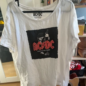 Vit AC/DC T-Shirt - Vit t-shirt från AC/DC med tryck av bandets logga och texten 'Shot in the Dark' på bröstet. Storlek XL 🌻