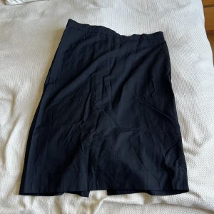 Svart långkjol från COS i ullmix - Stilren svart långkjol från COS i en skön ullmix med lite stretch. Kjolen har en klassisk rak passform och enkel design,Materialet är 98% ull och 2% elastan 