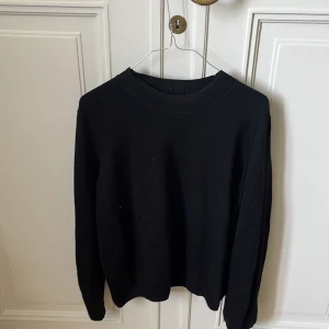 Svart tröja från COS i bomull - En stilren svart tröja från COS i storlek L. Tröjan har en bred ribbad rund halsringning och långa ärmar. Perfekt för dig som gillar minimalistisk och clean stil. Materialet är mjuk bomull som känns skönt mot huden.
