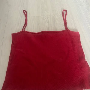 Röd ribbad kroppad linnetopp från H&M Divided - Säljer en röd ribbad linnetopp från H&M Divided i storlek XS. Toppen har smala axelband och är tillverkad i ett stretchigt material som sitter snyggt på kroppen. Perfekt för sommardagar eller att styla lager på lager.