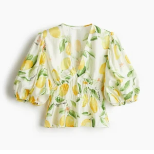Blommig blus med citrontema - Superfin blus med citrongult och grönt mönster på vit botten. Puffiga trekvartsärmar, v-ringad och smockad midja som ger en snygg siluett. Perfekt för dig som vill sticka ut med en färgglad och somrig vibe.