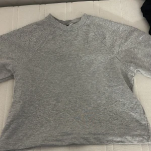 Grå sweatshirt från Gina Tricot - En basic grå sweatshirt från Gina Tricot i storlek M. Tröjan har rund halsringning, korta ärmar och är tillverkad i mjuk bomullsmix. Använd en gång.
