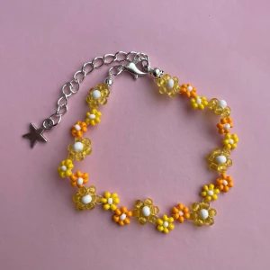 Handgjort färgglatt blommigt pärlarmband - Supergulligt armband med små blommor i pärlor, mixat i gult, orange och vitt. Armbandet har en silverfärgad kedja med stjärnberlock och justerbar längd. Perfekt accessoar för att liva upp din outfit med somrig vibe!