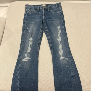 Blå slitna jeans från Gina Tricot - Snygga blå jeans från Gina Tricot i storlek 158. Jeansen har slitna detaljer framtill, klassisk femficksmodell och coola bakfickor med knapp och broderi. Raka ben och normal passform, perfekt till en avslappnad look.                                  Sms får mer bilder på.