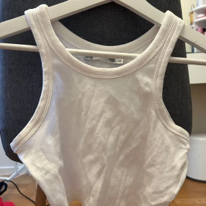 Vit ribbad linnetopp XS - Säljer en enkel och fräsch vit ribbad linnetopp i storlek XS. Toppen har breda axelband och rundad halsringning, perfekt för en clean och stilren look. Materialet är mjukt och stretchigt för extra komfort.