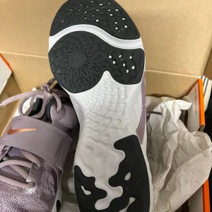 Nike Renew In-Season TR 12 lila sneakers - Nike Renew In-Season TR 12 sneakers i lila mesh med metallic kopparfärgade swoosh-detaljer. Skorna har snörning, bred rem över vristen och en vit sula med svarta detaljer. Perfekta för träning med snygg och sportig look.