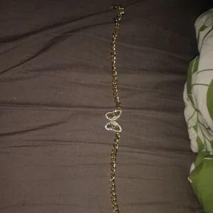Guldfärgat halsband med fjäril - Snyggt halsband i guldfärg med en stor, glittrig fjäril som hänge. Kedjan är grov och länkarna är ovala, vilket ger ett trendigt och iögonfallande intryck. Fjärilen är dekorerad med små stenar som glittrar fint i ljuset. Perfekt för dig som gillar statement-smycken.