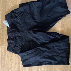 Svarta kostymbyxor med resår - Svarta kostymbyxor med elastisk midja och raka ben. Byxorna har diskreta fickor fram och bak, och är gjorda i ett mjukt tyg som känns bekvämt. Perfekta för en clean och stilren look.