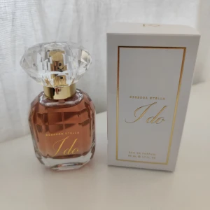 Rebecca Stella I do parfym 50ml - Lyxig parfym från Rebecca Stella, I do, i en elegant glasflaska med diamantformad transparent kork och guldiga detaljer. Doften är feminin och flaskan rymmer 50 ml. Kommer i stilren vit kartong med gulddetaljer. Endast testad!