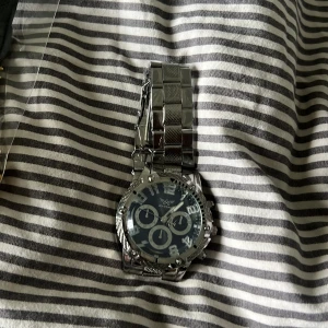 Stor silverfärgad klocka från Skone - Säljer en rejäl och snygg klocka från Skone med silverfärgat armband i metall och stor urtavla med tydliga siffror. Klockan har flera små urtavlor och en cool, sportig look som sticker ut på handleden. En är lite större