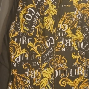 Versace Jeans Couture svart/gul jacka - Säljer en fet jacka från Versace Jeans Couture i svart med gult barockmönster och stora logotexter. Jackan har dragkedja framtill och är tillverkad i mjuk bomullsmix. Perfekt statement-plagg för dig som vill sticka ut. Köpte den runt 5000 kr bara testa den. Pris kan diskuteras 