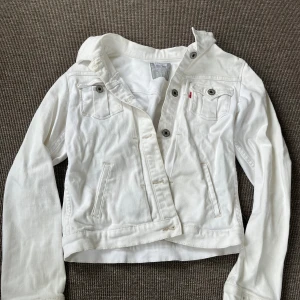 Vit jeansjacka från Levi's, stl 152-158 - Snygg vit jeansjacka från Levi's med klassiska bröstfickor och knappar framtill. Jackan har lång ärm, raka sömmar och en clean look som passar till allt. Perfekt för dig som vill ha en fräsch och stilren jacka till våren eller sommaren.