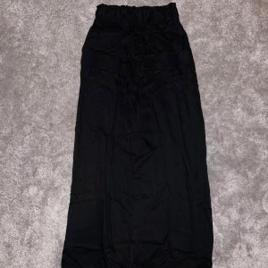 Svarta vida byxor med knytband - Säljer ett par svarta, vida byxor med hög midja och elastisk resår. Byxorna har ett snyggt knytband i midjan och är gjorda i ett lätt, flowy tyg som känns riktigt skönt. Perfekta för en chill och stilren look. Byxorna har bara använda en gång.