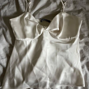 Vitt satinlinne från Gina Tricot - Supersnygg vit linnetopp från Gina Tricot i glansigt satinliknande material. Toppen har smala axelband och en snygg twist-detalj framtill vid bysten. 