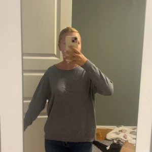 Grå basic tröja från Evelin - Enkel och stilren grå tröja från Evelin i mjukt material. Tröjan har rund halsringning, långa ärmar och en avslappnad passform. Perfekt att matcha med jeans eller kjol för en clean look.