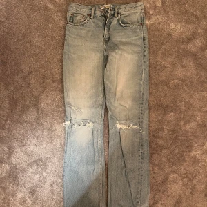 Ljusblå raka jeans från Zara - Säljer ett par ljusblå jeans från Zara med raka ben och slitna detaljer vid knäna. Klassisk femficksmodell med knapp och dragkedja. Perfekta för en avslappnad och trendig look.