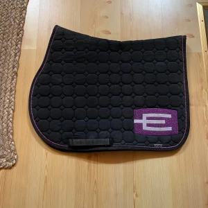 Equiline schabrak  - Svart/Lila glittrigt E logga schabrak, storlek Full. Jättebra skick. Är otvättat just nu men kan tvättas ifall köparen bestämt sig för att köpa de. Tvättar det helst inte i onödan. Nypris runt 2000kr 