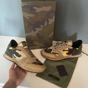 Valentino Rockrunner sneakers camouflage - Snygga Valentino Rockrunner sneakers med camouflage-mönster i beige, brunt, grönt och inslag av gult. Skorna har klassisk snörning, rund tå och detaljer i mocka och skinn. Perfekta för dig som vill sticka ut med exklusiva och trendiga sneakers. Tar byten också 