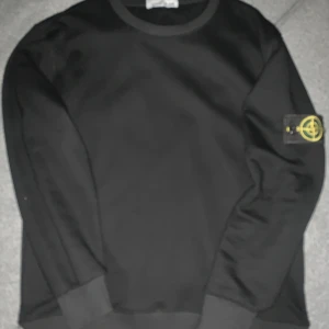 Svart Stone Island sweatshirt i bomull - Svart långärmad sweatshirt från Stone Island med klassisk rund hals och ikonisk logopatch på vänster ärm. Tillverkad i 100% bomull för en skön och avslappnad vibe. Perfekt för dig som gillar streetwear och stilrena plagg.