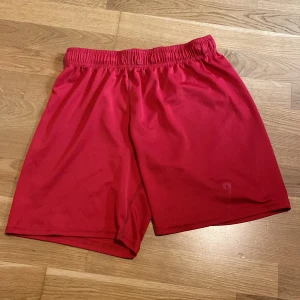 Röda sportshorts från H&M - Röda sportiga shorts från H&M med elastisk midja och tryckt siffra 7 på ena benet. Tillverkade i 100% polyester, perfekta för träning eller fotboll. Lätta och bekväma med loose fit för maximal rörelsefrihet.