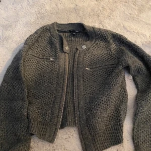 Mörkgrå stickad cardigan jacka - Mysig mörkgrå stickad cardigan jacka med grovstickat mönster, dragkedja framtill och två små fickor med dragkedja på bröstet. Ribbstickade muddar vid ärmslut och nederkant. Köpt på vinted men kommer inte till användning! 