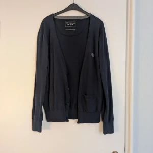 Mörkblå kofta från Cottonfield - Mörkblå kofta från Cottonfield med liten bröstlogga, knäppning framtill och en liten ficka. Tillverkad i mjuk bomullsblandning med polyamid för extra komfort. Perfekt för lager-på-lager och passar till allt. Klassisk och stilren look.