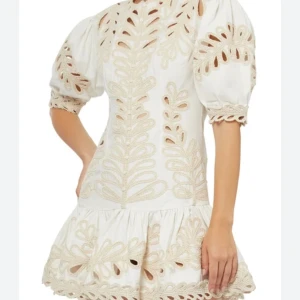 Vit kort klänning med broderi från maje - Superfin vit kort klänning från By Malina med puffärmar och broderade detaljer i beige. Klänningen har vackra utskärningar, volang nertill och rund hals. Perfekt för sommarens alla tillfällen och ger en riktigt fräsch look.