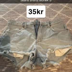 Ljusblå jeansshorts med fransar - Säljer ett par ljusblå jeansshorts med råa, fransiga kanter och klassisk femficksdesign. Shortsen har bälteshällor och knappgylf. Perfekta för varma dagar och en avslappnad stil.