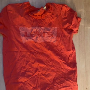 Röd Levi's t-shirt med logga - Snygg röd t-shirt från Levi's med klassisk logga tryckt framtill. T-shirten har korta ärmar och rund halsringning. Perfekt för dig som gillar streetwear och vill ha en enkel men ikonisk look.