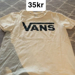 Vit Vans t-shirt med logga - Vit t-shirt från Vans med stor svart logga över bröstet. Klassisk rund halsringning och korta ärmar. Perfekt basic-plagg med streetkänsla, passar till jeans eller shorts.