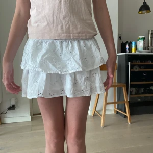 Vit volangkjol  - Supersöt vit kortkjol med två lager volanger och broderade hålmönster. Kjolen är i tunn bomull, perfekt för varma dagar. Den har en luftig och lätt känsla som gör den riktigt skön att 