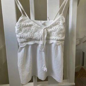 Vit virkad linnetopp  - Supersöt vit linnetopp från Stradivarius med virkade detaljer upptill och knyt framtill. Smala axelband och flowy, lätt skrynklig nederdel. Perfekt för varma dagar och ger en boho-vibe. Toppen har elastisk rygg för extra komfort.