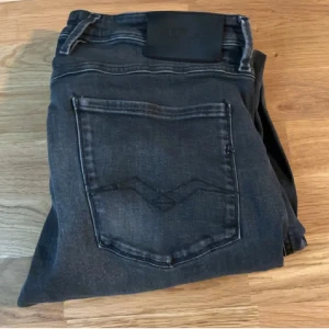 Replay svarta slim jeans - Snygga svarta jeans från Replay med diskreta slitningar och klassiska fem fickor. Jeansen har en slim passform och är tillverkade i stretchigt denim för extra komfort. Perfekta för dig som gillar en stilren look med lite edge.