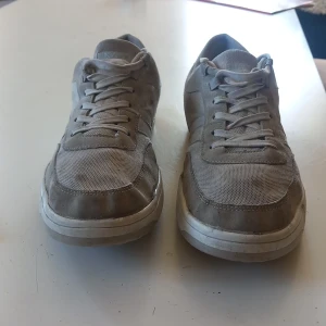Beige sneakers i mocka och mesh - Snygga beige sneakers med ovandel i mocka och mesh för en stilren look. Skorna har klassisk snörning och platt vit sula. Perfekta för dig som gillar en clean och enkel stil till vardags.