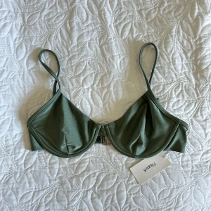 Grön bikiniöverdel från Filippa K - Snygg bikiniöverdel från Filippa K i en blekgrön nyans med lätt glans. Modellen har bygel, smala axelband och metallspänne bak. Perfekt för strandhäng och pooldagar. Materialet är mjukt och stretchigt syntet för bästa komfort.