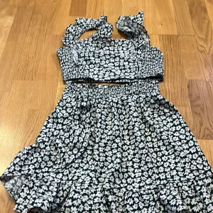 Blommig kortklänning med volang - Supersöt kortklänning med vita blommor på mörkgrön botten. Klänningen har volangdetaljer, smockad överdel och breda axelband med volang. Perfekt för sommarens alla tillfällen och ger en riktigt fräsch vibe.