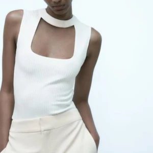 Vit ribbad ärmlös topp från Zara - Supersnygg vit ärmlös topp från Zara med ribbad struktur och unik fyrkantig cut-out vid halsen. Hög halsringning med bred krage och dragkedja bak. Perfekt för dig som gillar stilrena och trendiga plagg med det lilla extra.