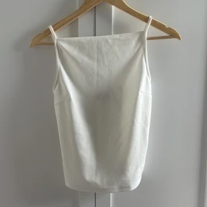 Vit topp från Gina Tricot - Säljer en gullig vit topp från Gina Tricot i storlek S. Toppen har tunna axelband och rak halsringning, perfekt för en clean och enkel look. Passar perfekt till jeans eller kjol. 48cm lång, aldrig använd!