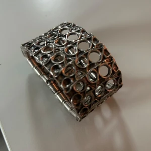 Brett silverfärgat armband med cirkelmönster - Unikt och brett armband i silverfärg med coolt cirkelmönster och industriell känsla. Armbandet har en öppen, luftig design med många olika stora hål och detaljerade kanter. Perfekt statement piece för dig som gillar att sticka ut.
