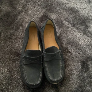 Svarta mockaloafers från Zapa - Stilrena svarta loafers i mocka från Zapa med klassisk design och ljus sula. Skorna har rund tå och diskreta sömmar framtill, perfekta för en clean och tidlös look. Passar dig som gillar enkel men snygg stil.