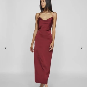 Vinröd långklänning med smala axelband - Vinröd långklänning i satinliknande material med smala axelband och figurnära passform. Klänningen har en elegant, enkel design med lätt draperad urringning och slät kjol. Perfekt för dig som vill ha en stilren och chic look. Använd en gång, nypris 459!