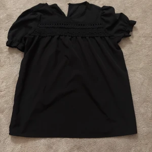 Svart blus med spetsdetaljer - Säljer en svart blus med puffiga korta ärmar och fina spetsdetaljer över bröstet.😍