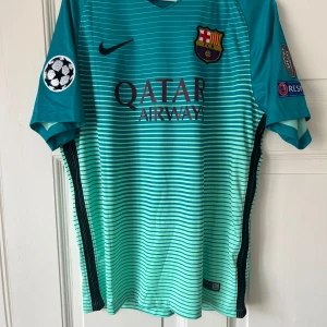 FC Barcelona Neymar Jr 11 bortatröja 2016 - Säljer en äkta FC Barcelona bortatröja från säsongen 2016 med Neymar Jr och nummer 11 på ryggen. Tröjan är turkos med tunna horisontella ränder, klubbmärke och Nike-logga på bröstet samt Champions League-patch på ärmen. Tillverkad i lätt och ventilerande polyester.