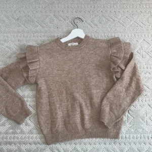 Beige stickad volangtröja från H&M - Supersöt beige stickad tröja från H&M med volangdetaljer på axlarna. Tröjan har rund halsringning, långa ärmar och ribbade muddar. Storlek 146/152 (nästan aldrig andvänd)💕💕