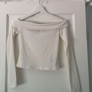 Vit offshoulder topp från H&M - Säljer en vit ribbad offshoulder topp från H&M. Toppen har långa ärmar och en snygg, bred kant som sitter över axlarna. Perfekt för dig som gillar stilrena och trendiga plagg med en enkel men chic vibe.