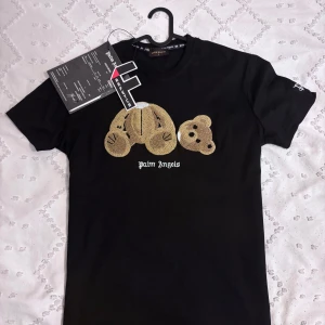 Palm Angels t-shirt - Svart t-shirt från Palm Angels med ikoniskt broderat björnmotiv på bröstet och vit logga under. Klassisk rund hals och korta ärmar. Tillverkad i mjuk bomull med lite stretch för extra komfort. Perfekt statement-plagg för dig som gillar streetwear.
