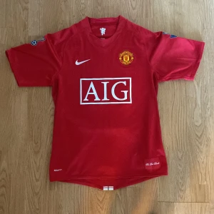 Manchester United Rooney 08/09 tröja - Klassisk Manchester United matchtröja från säsongen 07/08 med Rooney 10 på ryggen. Röd med vita detaljer, Premier League-märke på ärmarna och AIG som sponsor på bröstet. Tillverkad i lätt och ventilerande material, perfekt för fans och samlare. Trycket är lite slitet. Utöver det är tröjan äkta.
