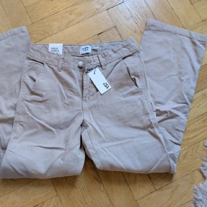Beige cargojeans - Helt nya! Ett par beiga cargo/workers jeans med raka ben och flera fickor både fram och bak. Byxorna har normal passform, bälteshällor och stängs med dragkedja och knapp. Perfekta för en avslappnad stil.